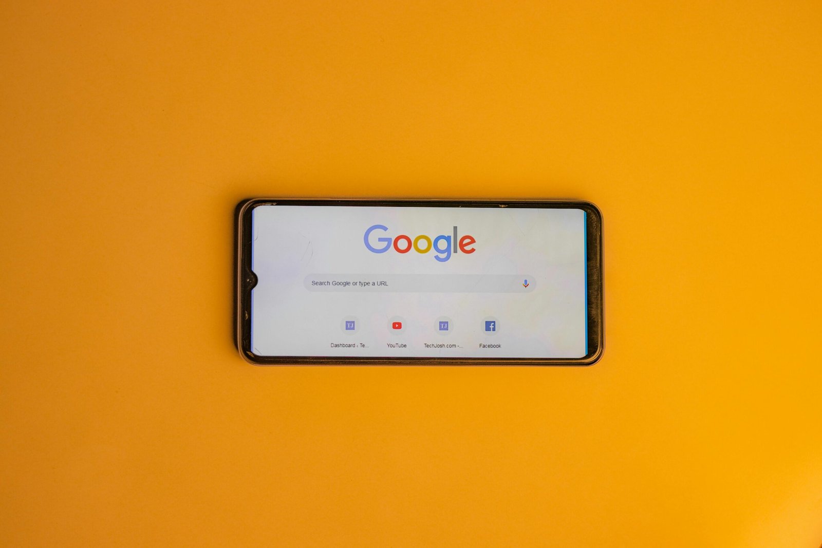 Smartphone displaying Google search page on a vibrant yellow background.